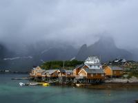 Leuchtende Rorbuhütten von Sakrisøy vor verhangenen Bergen - Lofoten